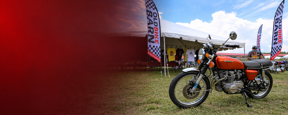 Vintage orange Honda motorcycle beside matching Old Bike Barn flags at a motorcycle show